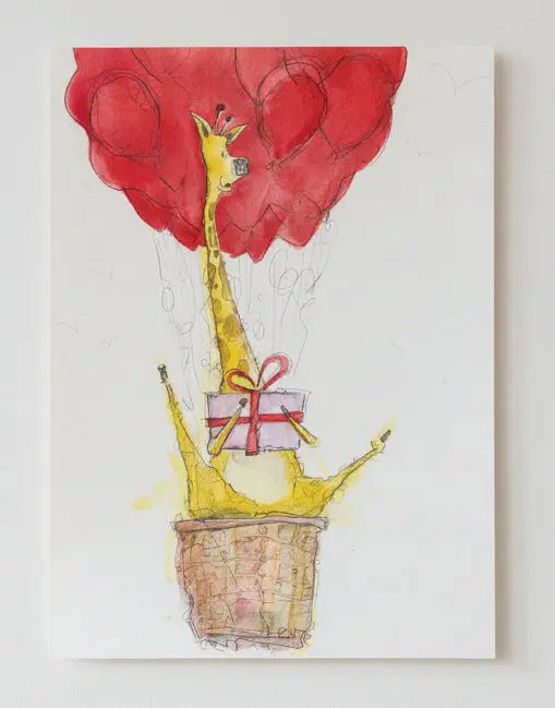 Framed artwork of a giraffe on a air balloon and a gift box on a textured wall.